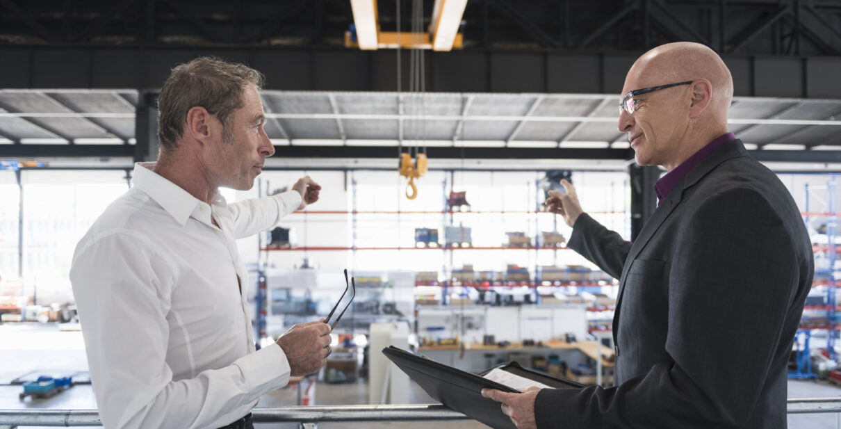 Two businessmen with clipboard talking on factory shop floor